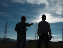 silhouette of two engineers standing at electricity station at sundown