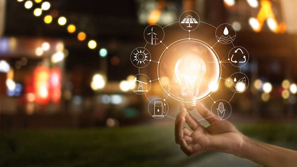 Hand holding light bulb in front of global show the world's consumption with icons energy sources for renewable, sustainable development. Ecology concept. Elements of this image furnished by NASA. 