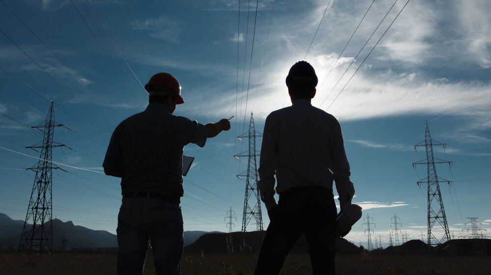 silhouette of two engineers standing at electricity station at sundown