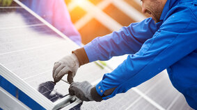Smiling male technician in blue suit installing photovoltaic blue solar modules with screw. Man electrician panel sun sustainable resources renewable energy source alternative innovation